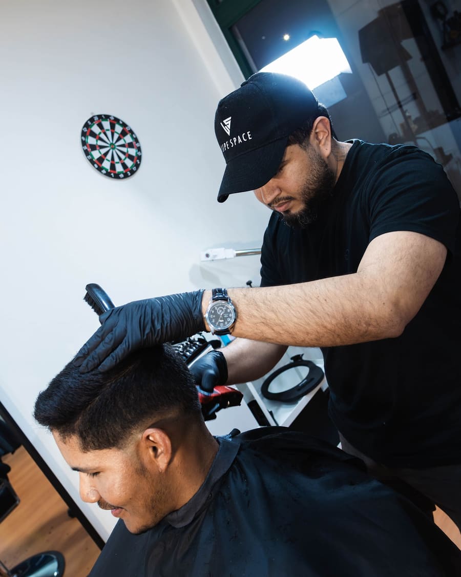 Felipe a acabar um corte à máquina, com o alvo de dardos na parede ao fundo